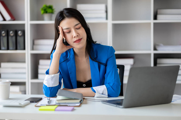 長時間労働や仕事の問題でストレスを受けている美しいアジアの女性、オフィス症候群を抱えている若いビジネス女性は、痛み、頭痛を引き起こします。オフィス症候群の概念. - 写真・画像