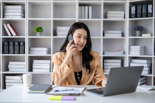 Gyönyörű ázsiai nő beszél a telefonon, üzletasszony dolgozik az irodában figyelmesen növekszik, és modernizálja az induló vállalkozás, ő elemzi a cég piaci és pénzügyi adatok. - Fotó, kép