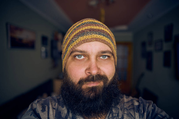 Een man met een baard met een gestreepte hoed en shirt, die opkijkt in de camera. - Foto, afbeelding