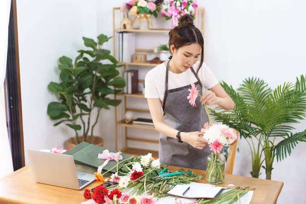 Florist concept, Female florist arranging pink gerbera and chrysanthemum in vase at flower shop. - Fotó, kép