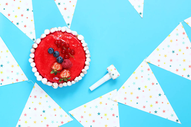 Festive gift cake on blue background, top view, flat lay. Birthday cake, festive horns and holiday flags. copy space - Zdjęcie, obraz