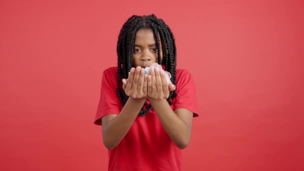 Happy Afryki kobieta dmuchanie confetti w studio z czerwonym tle - Materiał filmowy, wideo