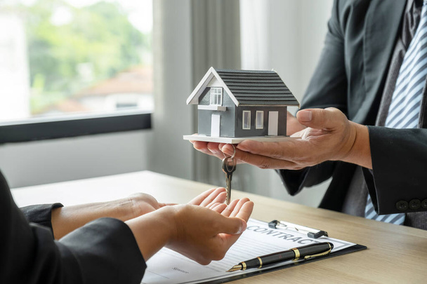 Immobilienmakler halten das Hausmodell in der Hand und erklären der Käuferin den Geschäftsvertrag, die Miete, den Kauf, die Hypothek, den Kredit oder die Hausversicherung. - Foto, Bild