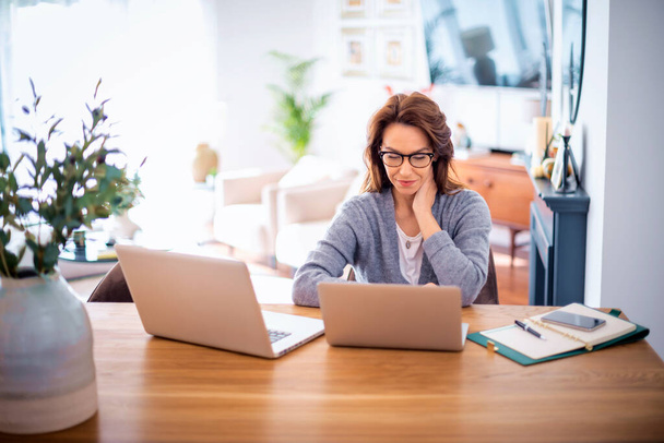 Attractive woman wearing eyewear and casual clothes while working from home. Business woman using laptops and having video call. Home office. - Foto, afbeelding