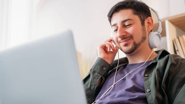 Music gadget. Song enjoyment. Device leisure. Joyful smiling carefree man listening mp3 tune playlist in headphones at modern laptop at home. - Φωτογραφία, εικόνα