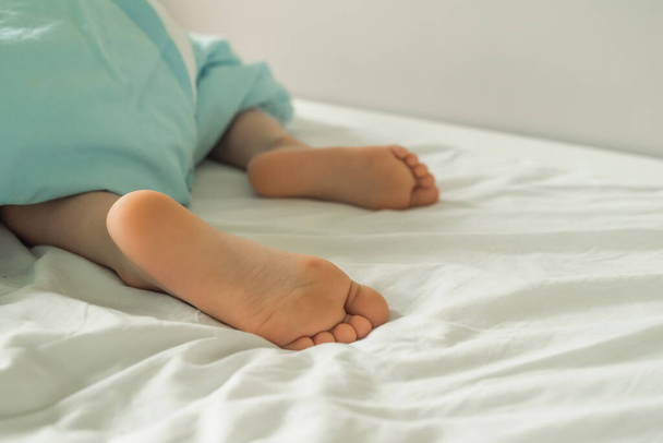 Children's legs stick out from under the blanket. A child's bed with protruding legs. Cute baby heels and toes - Foto, imagen