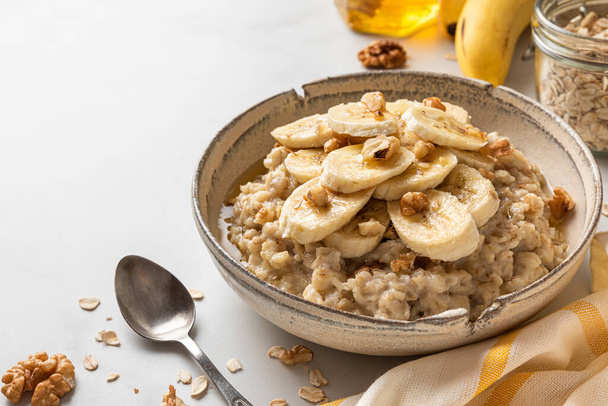 Bowl of oatmeal porridge with banana, honey and walnuts. Healthy diet breakfast. Close up - Photo, Image
