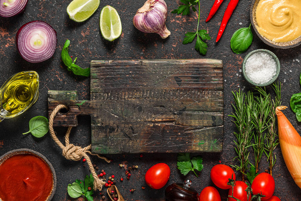 料理の背景。黒テーブルの上にまな板や道具とスパイス、ハーブや新鮮な野菜のフレーム。コピースペース付きのトップビュー - 写真・画像