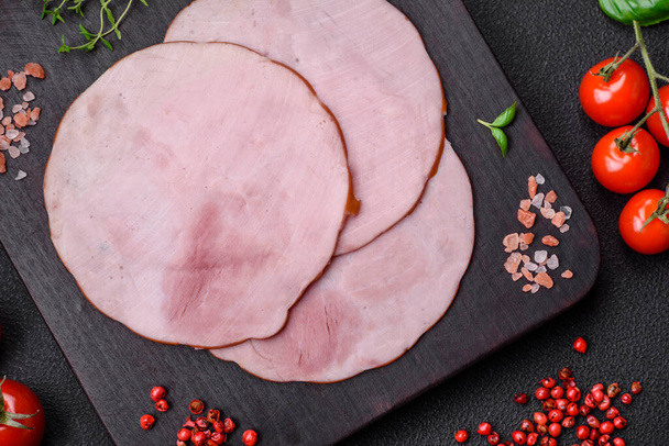 Delicious fresh ham cut into round slices with salt, spices and herbs on a dark concrete background - Φωτογραφία, εικόνα