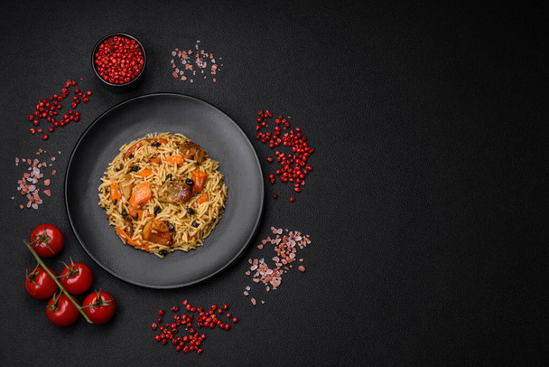 Delicioso pilaf fresco con arroz, zanahorias, carne, cebollas, especias y bayas en un plato de cerámica sobre un fondo de hormigón oscuro - Foto, imagen