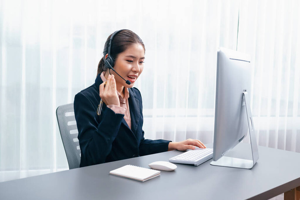 Asian call center with headset and microphone working on her laptop. Female operator provide exceptional customer service. Supportive call center agent helping customer on inquiry. Enthusiastic - Fotoğraf, Görsel