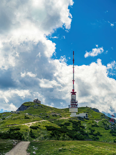 TV radio tower and chapel on the top of the mountain Dobratsch in Carinthia, Austria, summer, cloudy dramatic sky, wildflowers alpine landscape - Photo, Image
