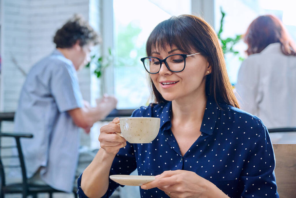 Relaxed happy middle aged woman enjoying fragrant fresh tasty cup of coffee while sitting in coffee shop. Coffee culture, lifestyle, people concept - 写真・画像