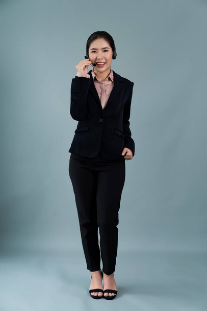 Attractive full body asian female call center operator with happy face advertises job opportunity on empty space, wearing formal suit and headset on customizable isolated background. Enthusiastic - Fotografie, Obrázek