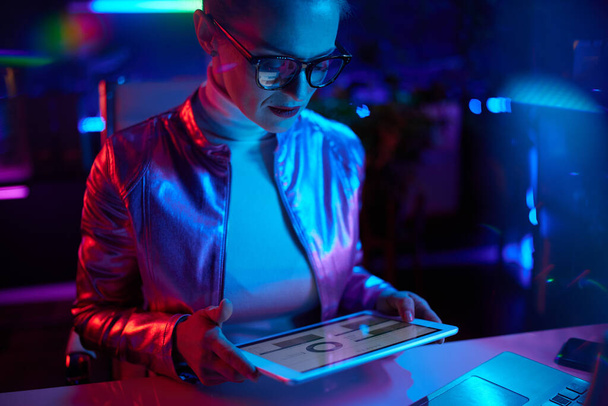 Neon metaverse futuristic concept. stylish woman in glasses with tablet PC working with charts in modern office. - Valokuva, kuva