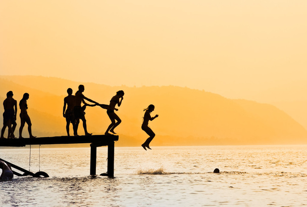 Силуети дітей, які стрибають з причалу на озері
 - Фото, зображення