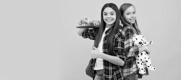 School girls friends. happy teen girls in casual checkered shirt carry backpack toy and penny board, skateboard. Portrait of schoolgirl student, studio banner header. School child face, copyspace - Fotoğraf, Görsel