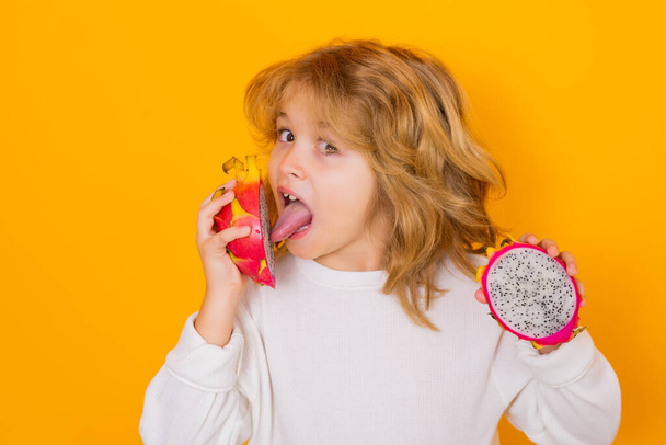 Kid eat dragon fruit in studio. Studio portrait of cute child with dragon fruit isolated on yellow background - Fotó, kép