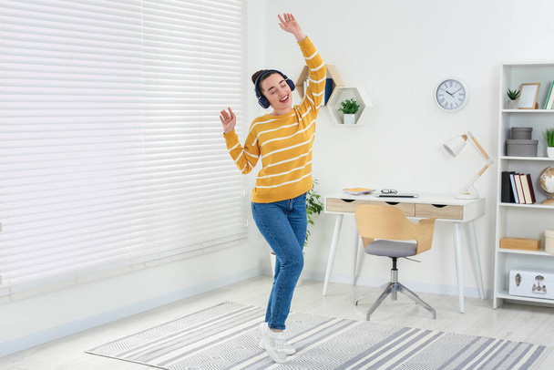 Happy woman in headphones listening music and dancing in cosy room - Foto, Imagen