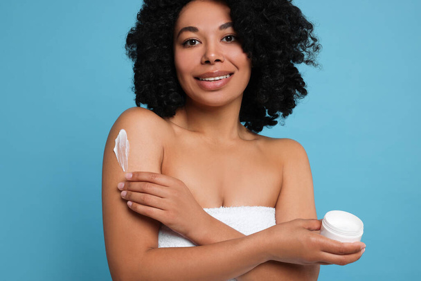 Young woman applying body cream onto shoulder on light blue background - Photo, Image
