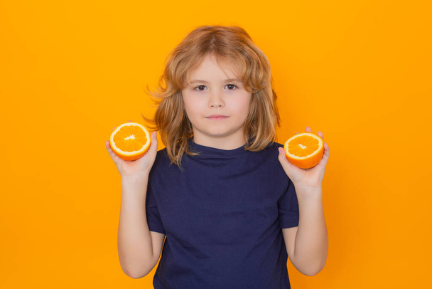 Kid with orange in studio. Studio portrait of cute child hold orange isolated on yellow background - Φωτογραφία, εικόνα