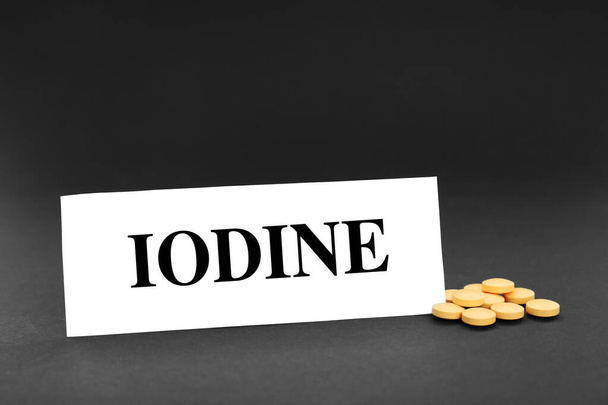 Carte avec mot Iode et pile de pilules sur fond noir - Photo, image