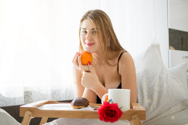 beautiful young woman lying in bed and holding orange - Photo, Image