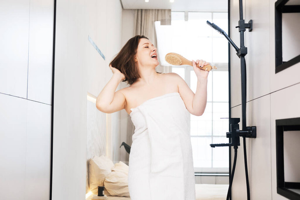 Cheerful plump woman singing in the shower using a brush as a microphone. Lifestyle concept. - Φωτογραφία, εικόνα
