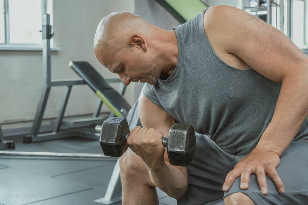 Hombre musculoso haciendo un ejercicio con una mancuerna para bombear bíceps en el gimnasio. Primer plano - Foto, imagen