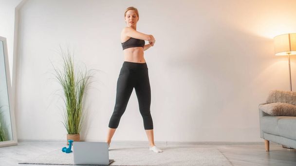 Internet fitness. Online gym. Digital workout. Athletic woman stretching watching video sport training on laptop at light home interior with copy space. - Zdjęcie, obraz