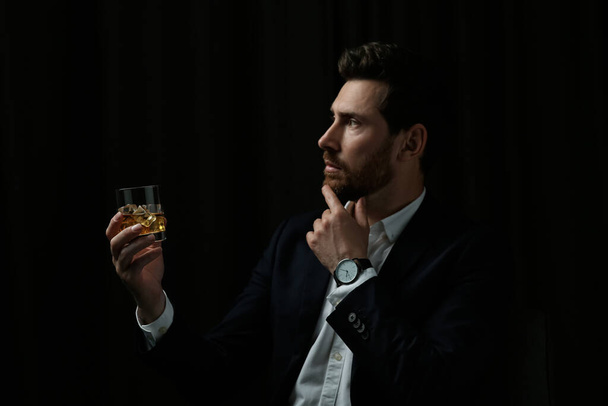 Handsome man in suit holding glass of whiskey on black background - Φωτογραφία, εικόνα