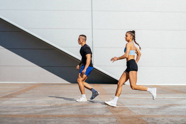 Dos atletas atractivos, una pareja, están corriendo juntos afuera, en un hermoso día soleado - Foto, imagen
