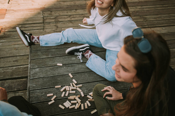 Close up of friends sitting on the wooden bench with scattered jenga - Photo, Image