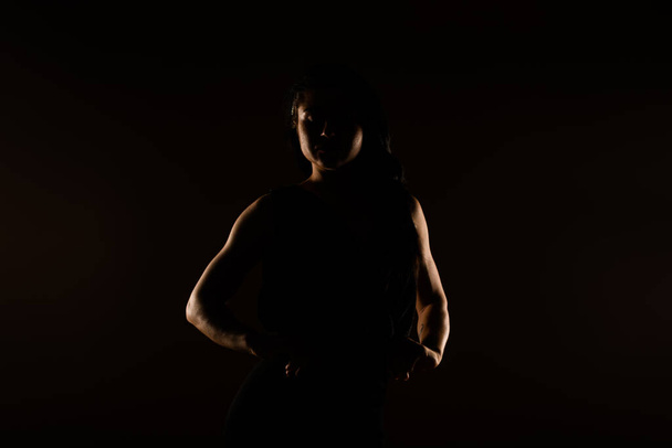 Lovely sporty girl posing in studoi in black dress. She is looking down. Hands on spine - Фото, зображення