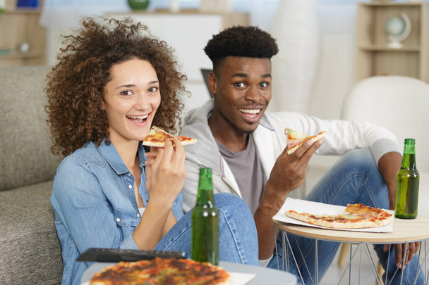 happy couple watching tv while eating pizza - Фото, зображення
