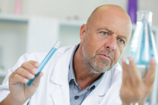 mature male scientist examining liquid in erlenmeyer flask - Фото, изображение