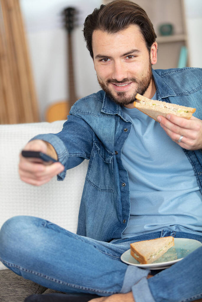 man changing tv channel while eating a sandwich - Zdjęcie, obraz