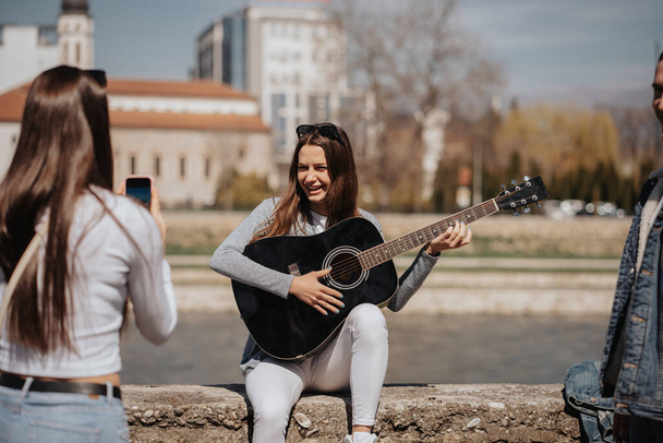 Beautiful girl is playing guitar while her friend is taking a photo of her - Photo, Image