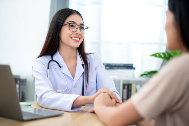 Beautiful female doctor holding female patient's hand to encourage medical treatment and health care at clinic. Health care concept. - Photo, Image