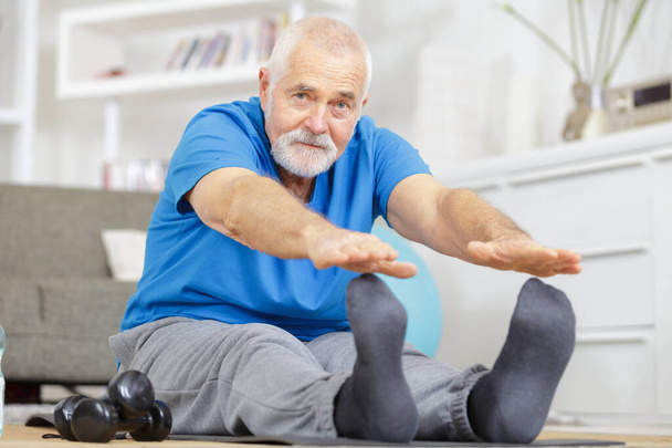 joyful senior stretching his legs at home - Photo, image