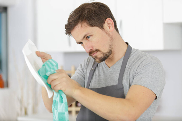 jonge huishoudster man tijdens het afwassen - Foto, afbeelding