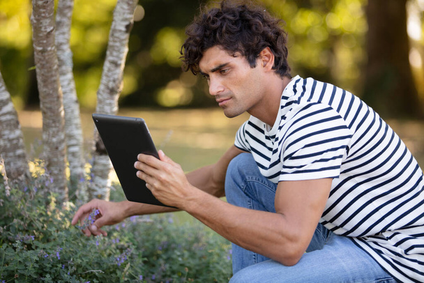 handsome man holding a tablet looking for plant references - Foto, afbeelding