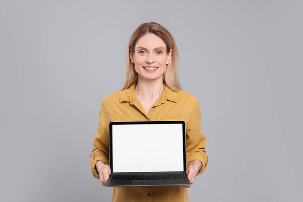 Happy woman showing laptop on light grey background - Valokuva, kuva