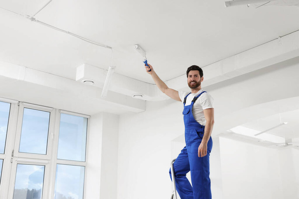 Handyman painting ceiling with roller on step ladder in room - Fotó, kép