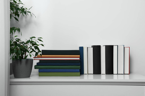 Many different books and potted plant on white cabinet indoors - Foto, imagen
