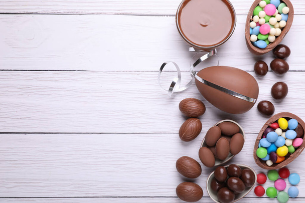 Delicious chocolate eggs, paste and candies on white wooden table, flat lay. Space for text - Fotografie, Obrázek