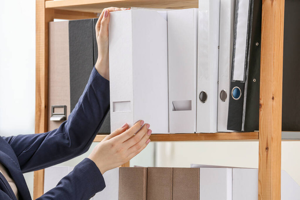 Woman taking folder with documents from shelf in office, closeup - Foto, immagini