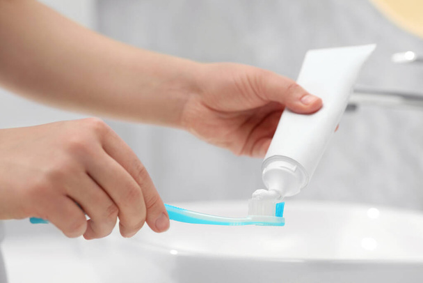 Woman squeezing toothpaste from tube onto toothbrush near sink in bathroom, closeup - Foto, Imagen
