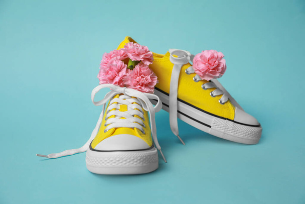 Pair of yellow classic old school sneakers and flowers on light blue background - Foto, Bild