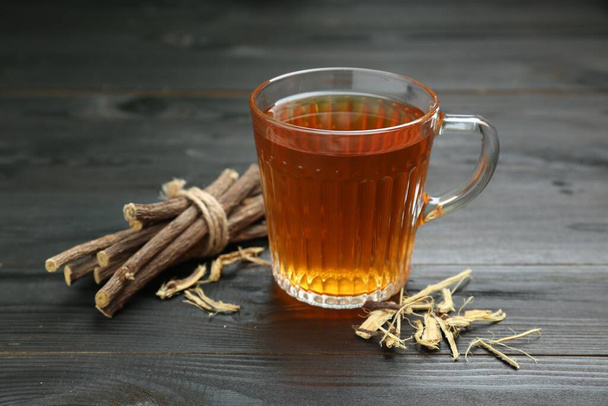 Aromatic licorice tea in cup and dried sticks of licorice root on black wooden table - Photo, image